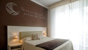 A neatly made bed with a headboard, two bedside lamps, and a decorative wall with a crescent moon and text. - Hotel Bel Sit (Alassio)