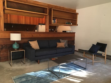 The living room with new sofa, leather chair, and tables. Galley kitchen beyond.