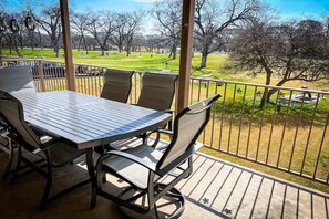 Une terrasse extérieure couverte, dotée d’une table et de chaises, qui offre une vue sur un parc arboré et verdoyant.