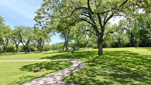 A park with a paved walkway, trees, and a sign. - Riverside Retreat | Riverfront | King Bed | Two Pools (New Braunfels)