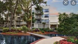 A modern hotel with a swimming pool, surrounded by landscaped gardens and palm trees.