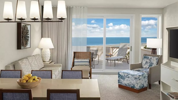 A hotel room with a balcony, a dining area, a seating area, and a TV.
