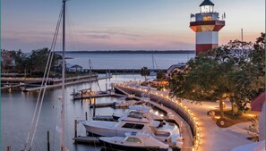 Ein Yachthafen am Wasser mit vertäuten Booten, einem Leuchtturm und einem gut beleuchteten Weg.