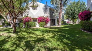 A two-story house with a well-maintained lawn, flowering bushes, and a clear sky.