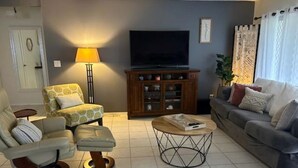 A living room with a sofa, armchair, ottoman, coffee table, TV, cabinet, and a lamp.