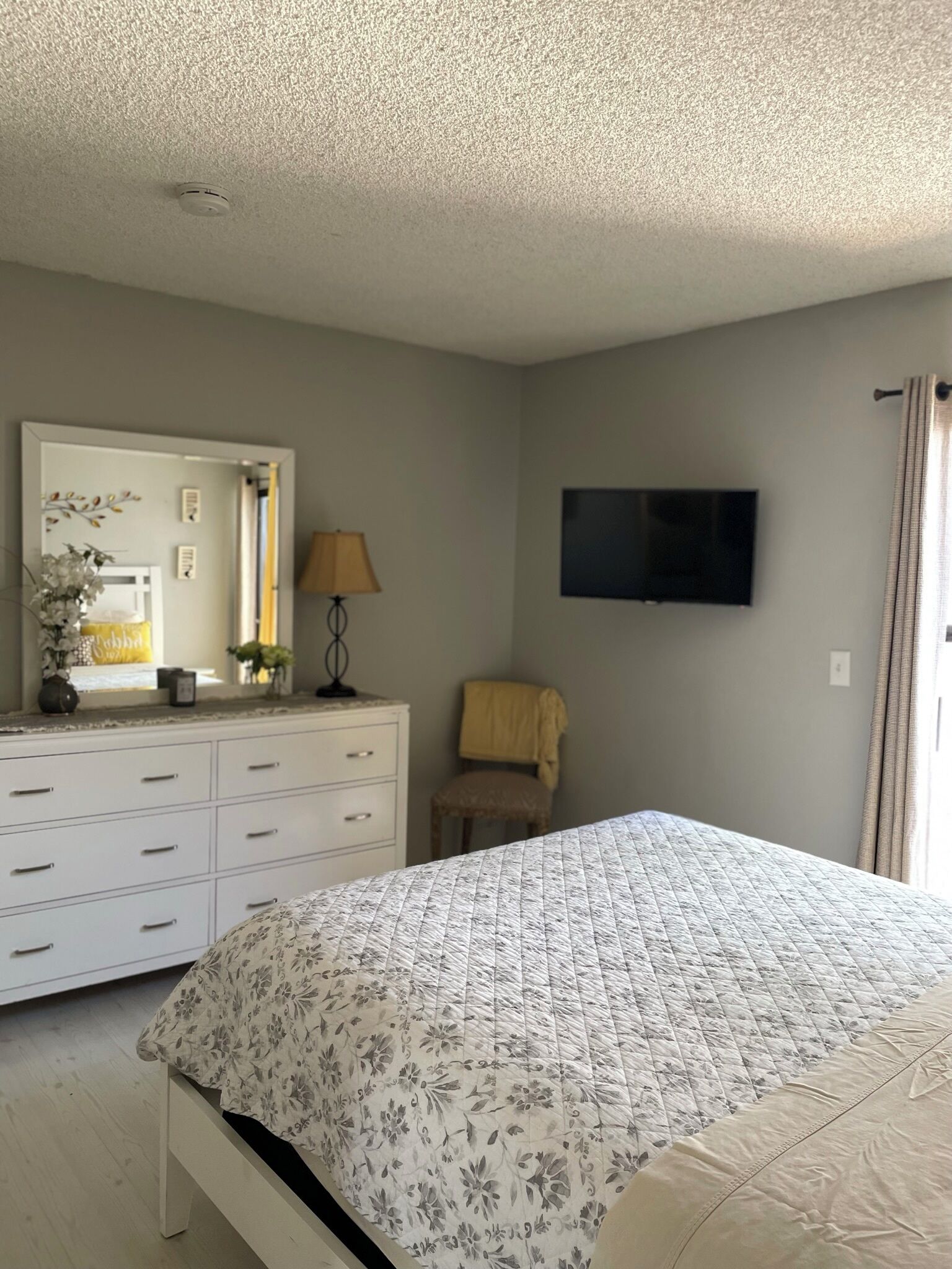 A bedroom with a bed, dresser, mirror, lamp, chair, and TV.