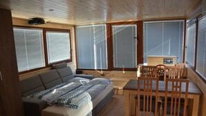 A cozy cabin interior with a sofa, dining table, and chairs. - Houseboat Bonanza in Prague - Bed & Cruise (Praha 7)