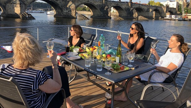 A group of people dining on a boat with a historic stone bridge in the background. - Houseboat Bonanza in Prague - Bed & Cruise (Praha 7)
