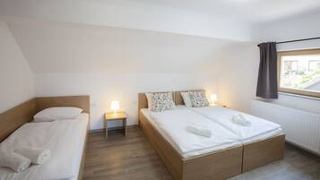 A hotel room with two single beds, a large bed, a window with curtains, and a nightstand with a lamp.
