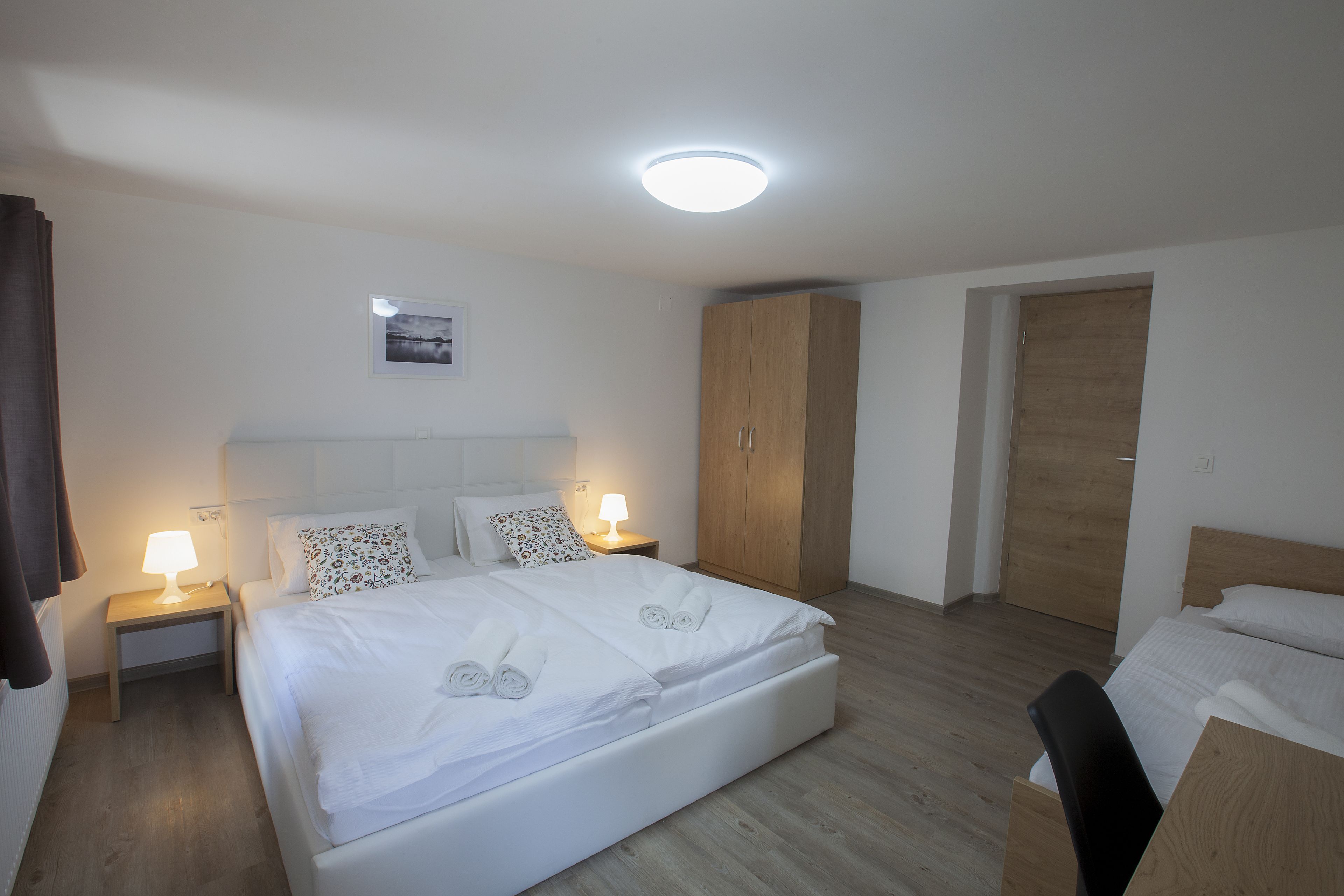 A hotel room with a large bed, bedside tables with lamps, a wooden wardrobe, and a door.