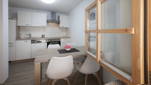 Une cuisine de taille réduite avec des meubles blancs, une table à manger en bois et deux chaises.