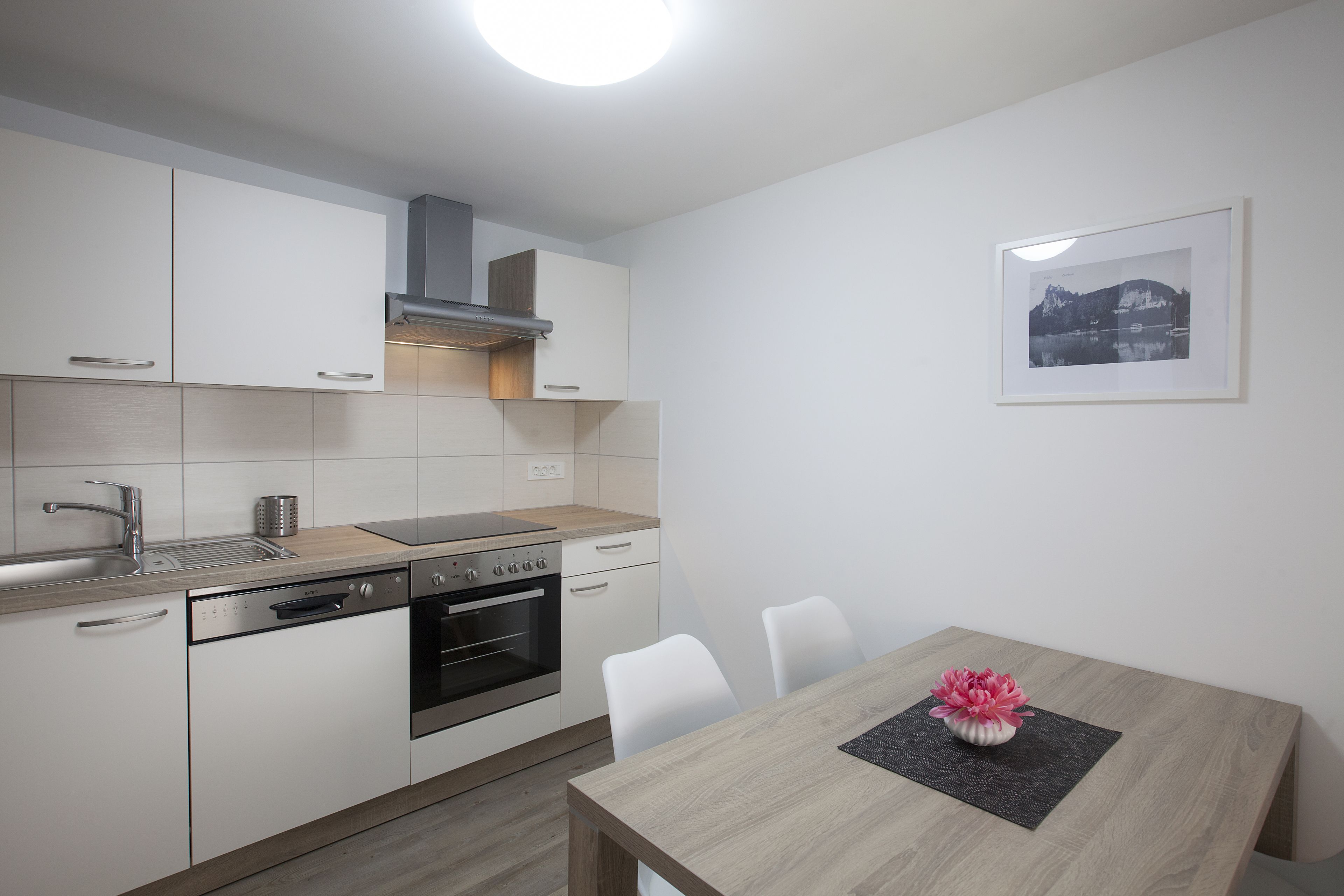 Una cocina moderna con armarios blancos, horno integrado y comedor con mesa y sillas de madera.