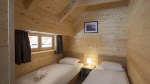 Une cabine équipée de deux lits simples, d’une fenêtre avec des rideaux, d’un tableau encadré au mur et d’une table de chevet avec une lampe.