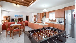 A spacious kitchen with wooden cabinets, a central island, and a foosball table. - Naxos Cottage - Cottage 1 (Naxos)