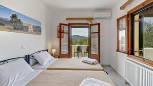 A bedroom with two beds, a balcony with chairs, and a painting on the wall. - Naxos Cottage - Cottage 1 (Naxos)