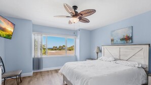 Un dormitorio con cama, ventilador de techo, ventana con vistas y un cuadro en la pared.