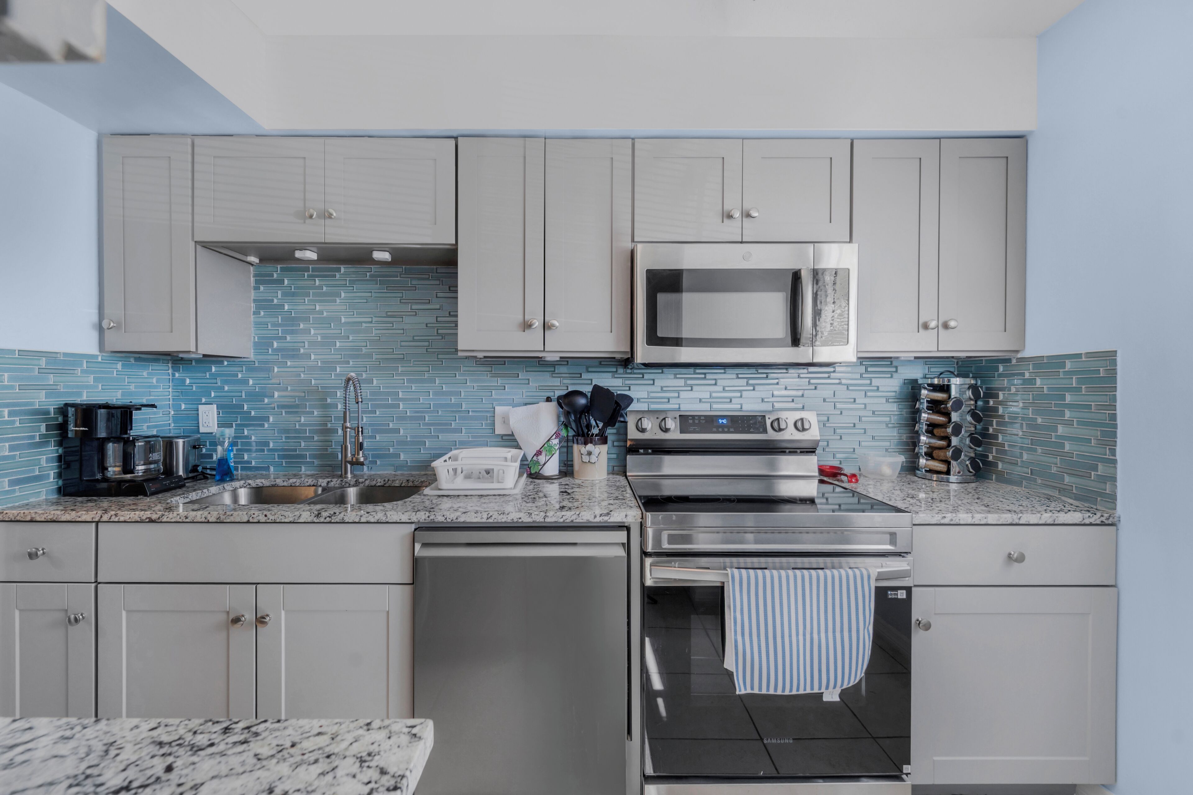 A modern kitchen with grey cabinets, a stainless steel microwave, an oven, and a dishwasher.
