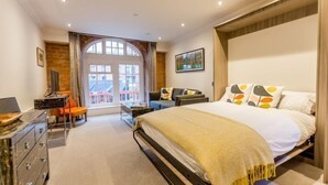 A modern bedroom with a large bed, a desk with a laptop, a chair, and a view of a building outside. - Cocoa Suites 5 - sleeps 2 guests  in studio apartment (York)