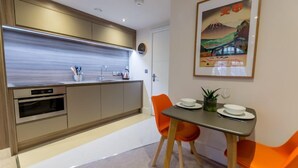 A modern kitchen with built-in appliances, a dining area with orange chairs, and a framed artwork on the wall. - Cocoa Suites 5 - sleeps 2 guests  in studio apartment (York)