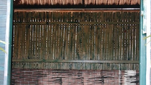 A wooden table with blue cushioned chairs in a covered outdoor area with a bamboo screen in the background. - Elite Inn (Bengaluru)
