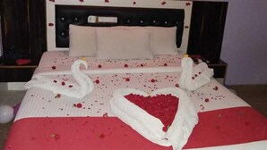 A bed with a red and white bedspread, a heart-shaped arrangement of rose petals, and two swan-shaped pillows. - Elite Inn (Bengaluru)