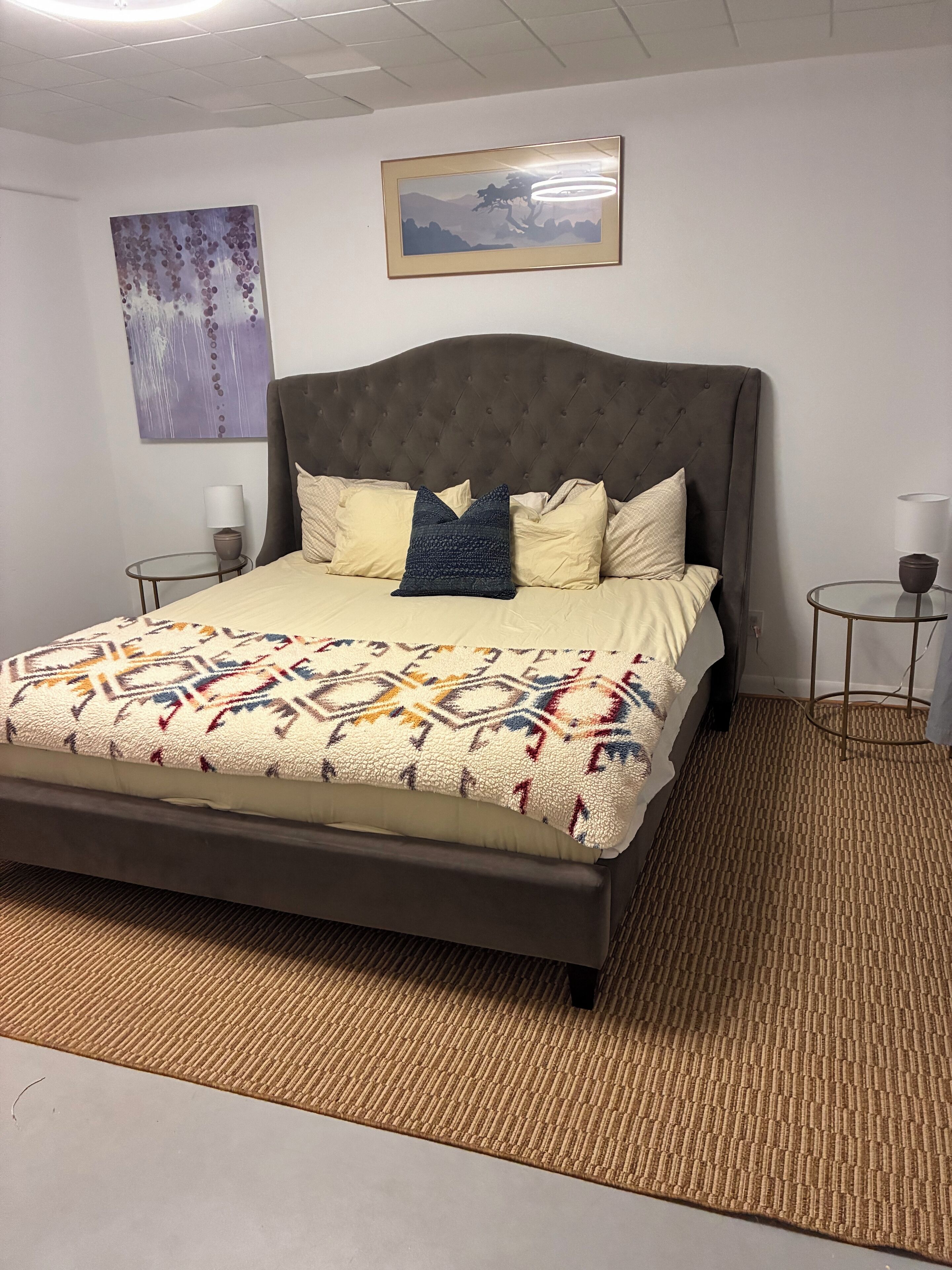 Un dormitorio ordenado con una cama grande, una manta estampada y dos mesitas de noche con lámparas.