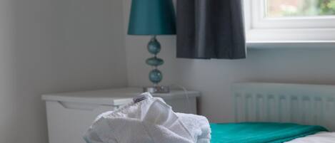 A neatly made bed with a teal blanket and a folded white towel on it.