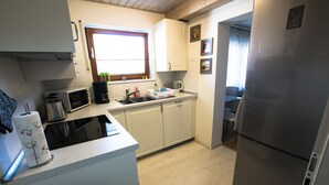 A compact kitchen with white cabinets, a stainless steel refrigerator, a microwave, a coffee maker, and a window with curtains. - Haus Steinberg (DTV 3 Sterne) - Herbi's holiday apartment - Ground floor   (Burladingen)
