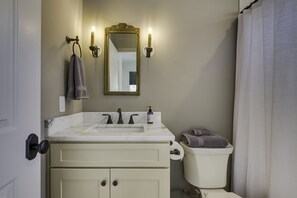 Une salle de bain avec un lavabo en marbre, des toilettes et un miroir agrémenté d’appliques murales.