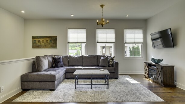 A living room with a sectional sofa, a coffee table, a chandelier, and a flat-screen TV mounted on the wall. - The Perfect Hideaway - Plan Your 30 Day Escape (Nashville)