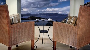 A wicker chair and table set on a balcony with a view of a lake and mountains. - Beautiful seaview villa with private sea water pool (Agios Nikolaos)