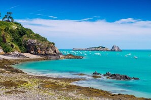 Eine Küstenlandschaft mit felsigem Gelände, klarem türkisblauem Wasser und Booten, die in der Ferne vor Anker liegen.