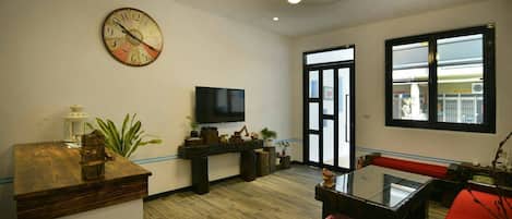 A modern living room with a wooden coffee table, a red sofa, a large wall clock, a flat-screen TV, and a large window with a view.