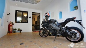 Una motocicleta estacionada en el interior, con piso de baldosas, pared de piedra decorativa y una puerta que da a otra habitación.