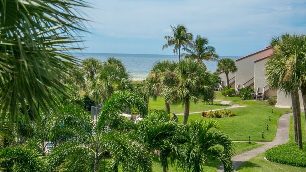 A resort with a view of the ocean, palm trees, and a pathway leading to a building with a red roof. - Renovated, Gulf View Unit, Overlooking the Pool and Beautiful Courtyard (Sarasota)