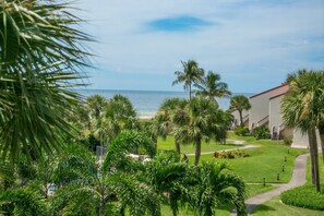 A resort with a view of the ocean, palm trees, and a pathway leading to a building with a red roof. - Renovated, Gulf View Unit, Overlooking the Pool and Beautiful Courtyard (Sarasota)