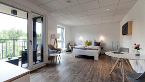 A modern, well-lit bedroom with a large bed, bedside tables, a small desk, and a balcony with outdoor seating.