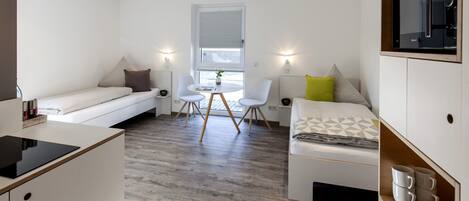 A compact hotel room with a kitchenette, a sofa, a bed, and a dining area.