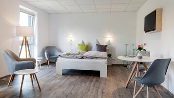 Een moderne slaapkamer met een bed, twee stoelen, een tafeltje, een televisie en een raam.