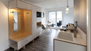 A modern hotel room with a built-in desk, a large mirror, a microwave, and a view of the outdoors.