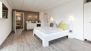 A modern bedroom with a large bed, a small bedside table, and a nightstand. There is a built-in wardrobe and a bathroom visible through an open door.