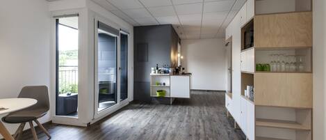 A modern kitchen with a wooden floor, a built-in white cabinet, and a glass door leading to a balcony.