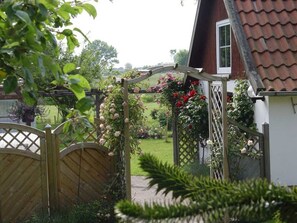 A wooden gate leading to a garden with a white building and a red-tiled roof.