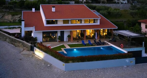 A modern two-story house with a swimming pool, outdoor seating, and a well-maintained garden.