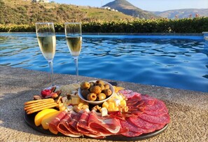 A charcuterie board with various meats, cheeses, and fruits by a pool with a mountainous backdrop. - 6 bedrooms/suites, infinity pool, gymnasium, gardens, barbecue - Douro Valley (São Cristovão do Douro)