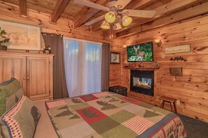 A cozy cabin interior with a bed, a fireplace, a television, and a ceiling fan. - ClearView: MtnView! Hot Tub, Wifi, Game Room, Resort Pool, near Dollywood (Sevierville)