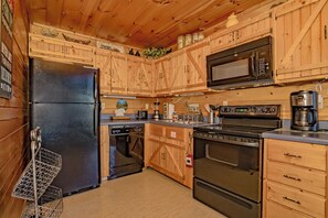 A kitchen with wooden cabinets, a black refrigerator, a microwave, a stove, and a coffee maker. - ClearView: MtnView! Hot Tub, Wifi, Game Room, Resort Pool, near Dollywood (Sevierville)