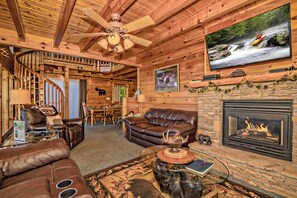 A log cabin interior with a fireplace, leather furniture, a television, and a ceiling fan. - ClearView: MtnView! Hot Tub, Wifi, Game Room, Resort Pool, near Dollywood (Sevierville)