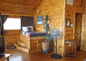 Una habitación de cabaña acogedora con una cama, un ventilador, una mesita pequeña y un televisor.