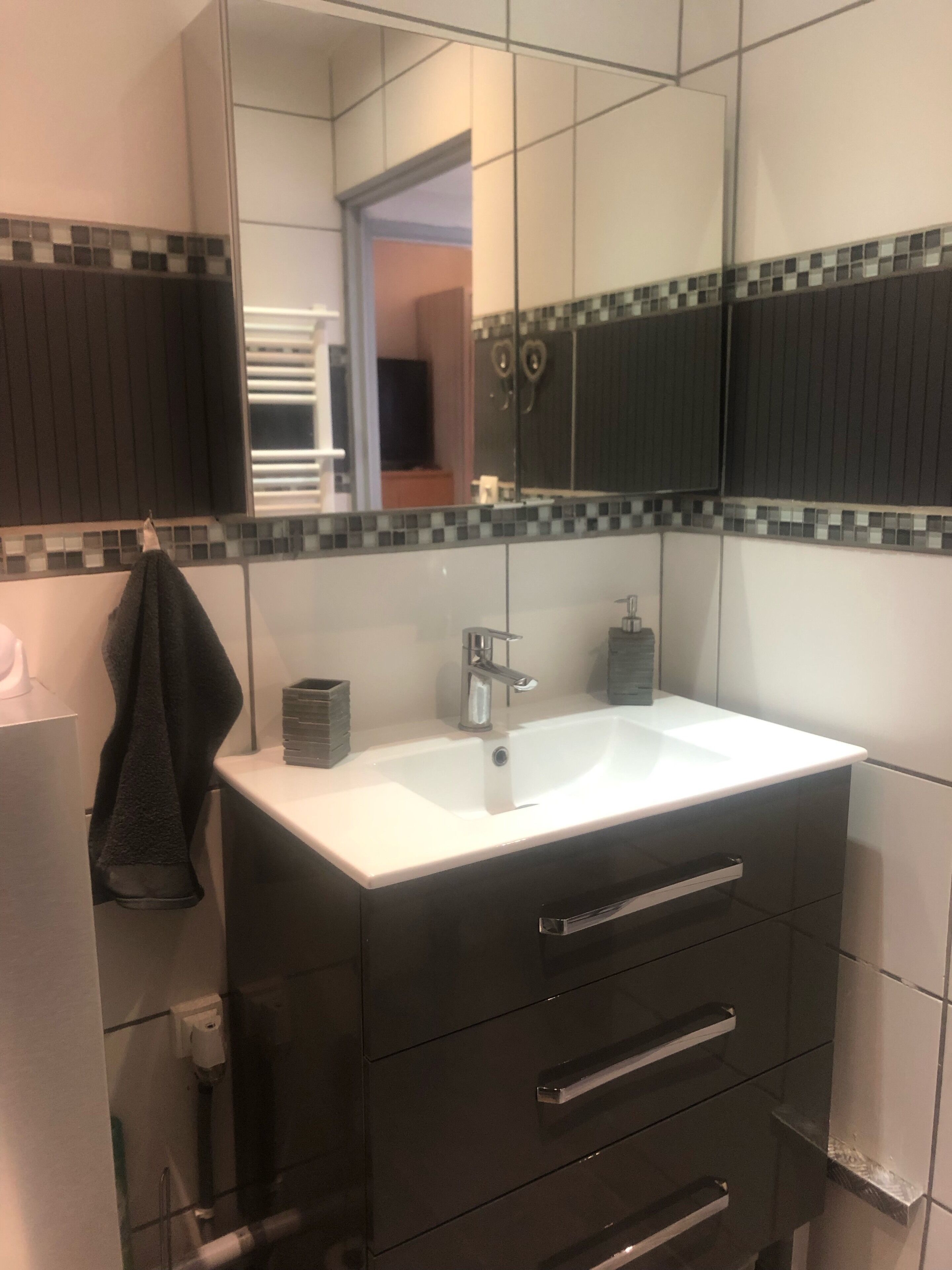 A bathroom with a white sink, dark cabinetry, and a tiled backsplash.